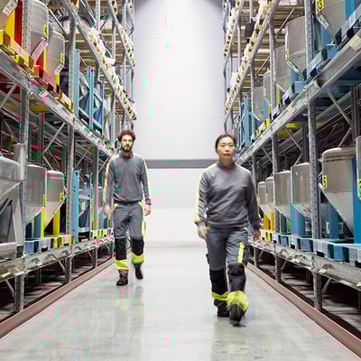 A man and a woman in work clothes walking between two warehouse shelves