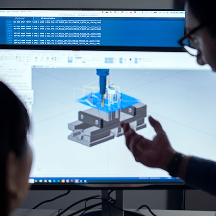 The heads of a woman and a man next to a computer screen displaying software simulating machining operation